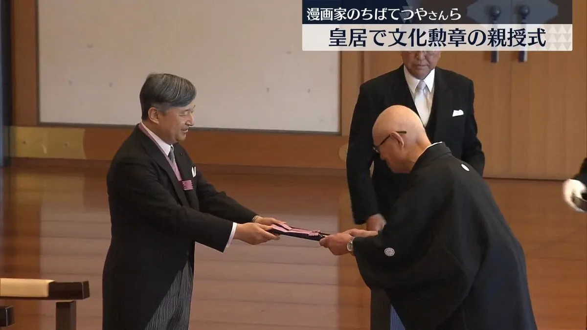 Capture d'un journal télévisé japonais : dans une salle du palais impérial, l'empereur en jaquette remet un insigne dans un étui à un homme en kimono noir à blason, qui s'incline.