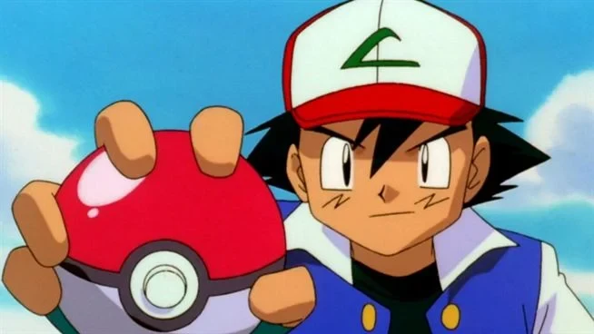 Sacha, casquette rouge et blanche sur la tête, tend une Poké Ball dans l’anime Pokémon