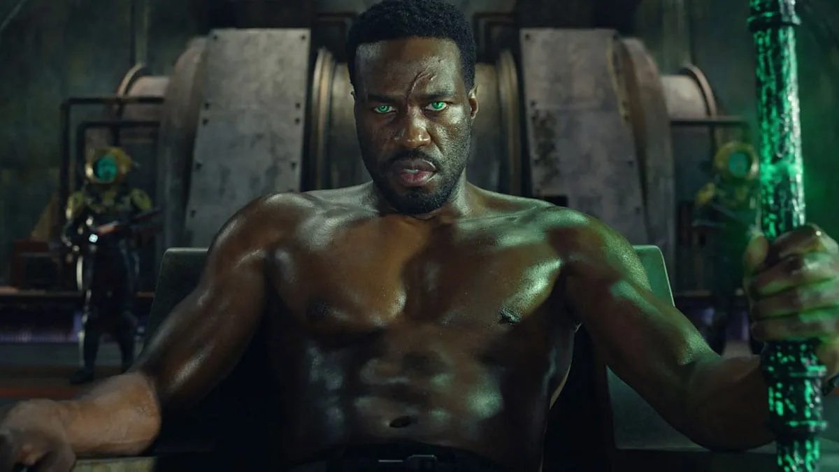 Yahya Abdul-Mateen II en Black Manta, yeux verts luisants, assis la main sur un trident noir