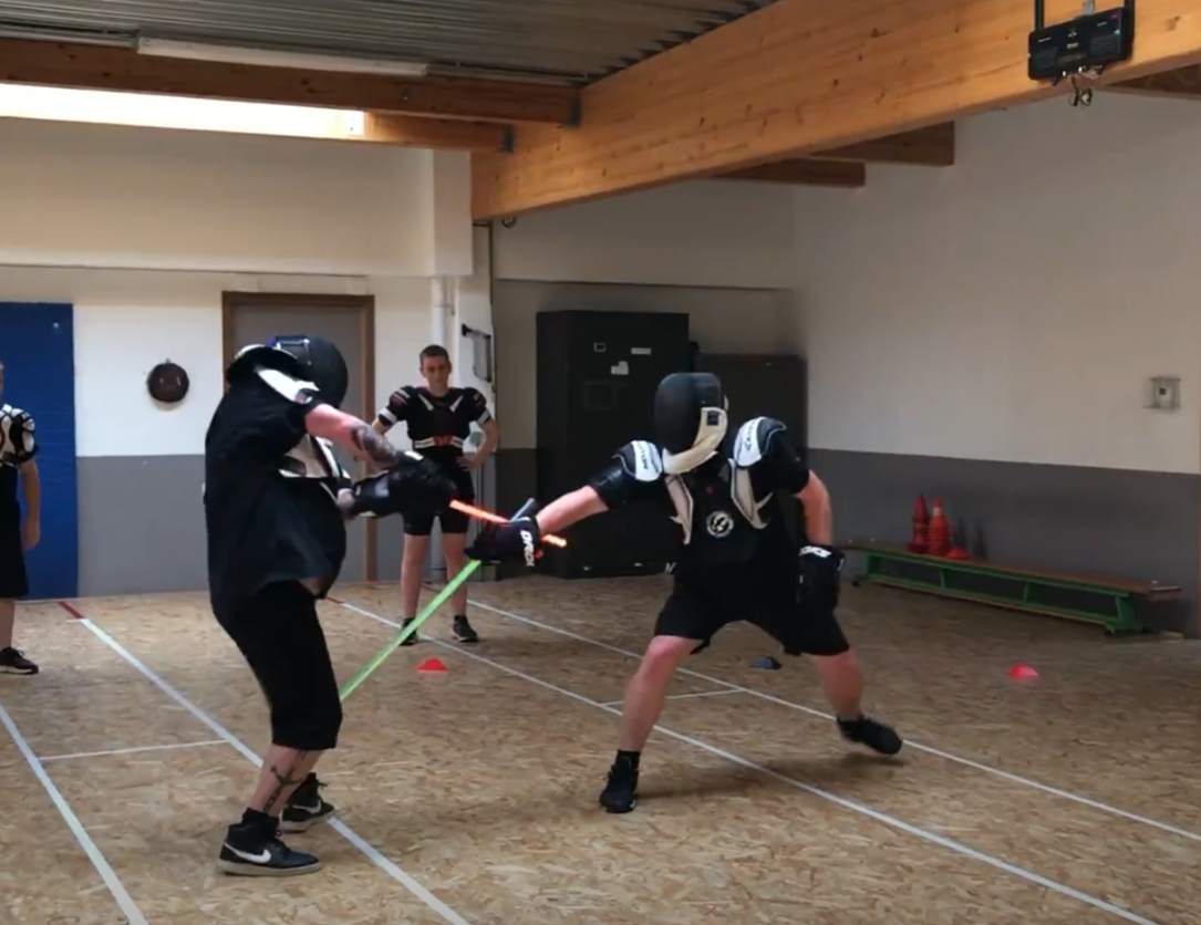 Deux combattants casqués s’affrontent au sabre laser dans une salle d’entraînement