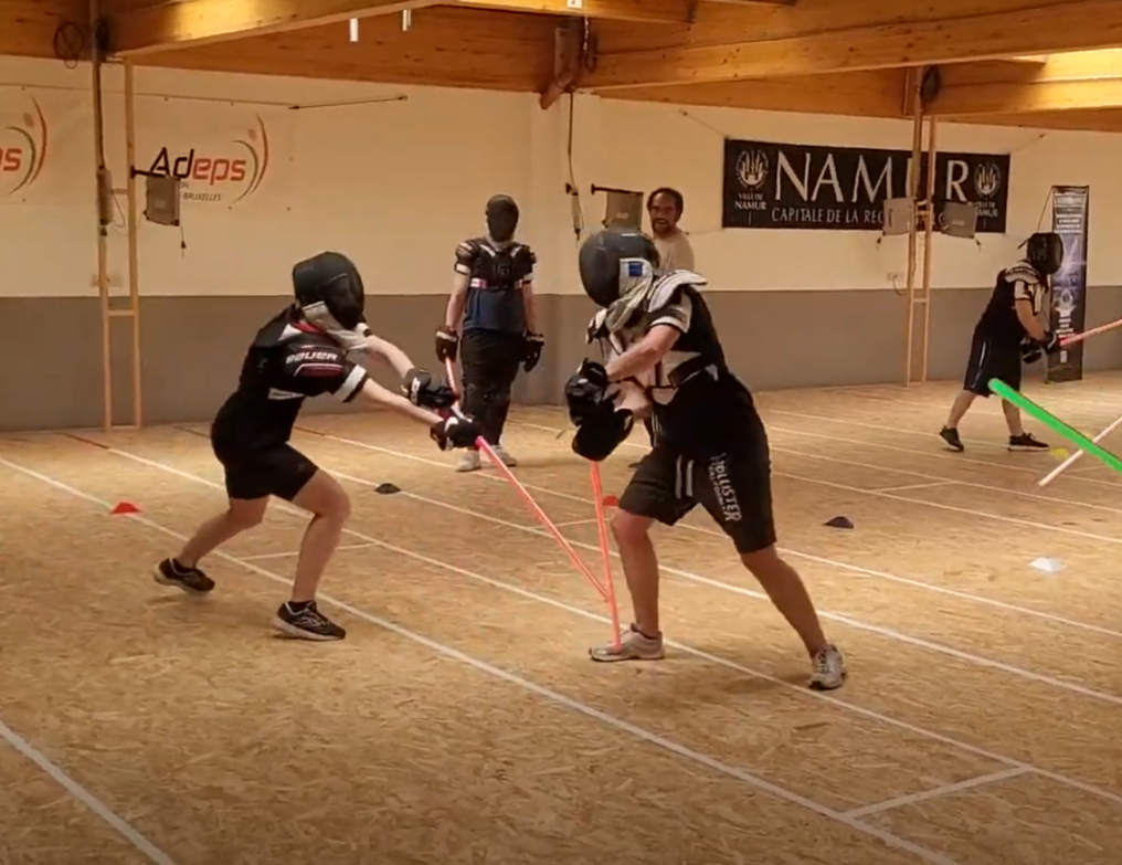 Duel au sabre laser entre deux jeunes combattants casqués dans une salle de Namur