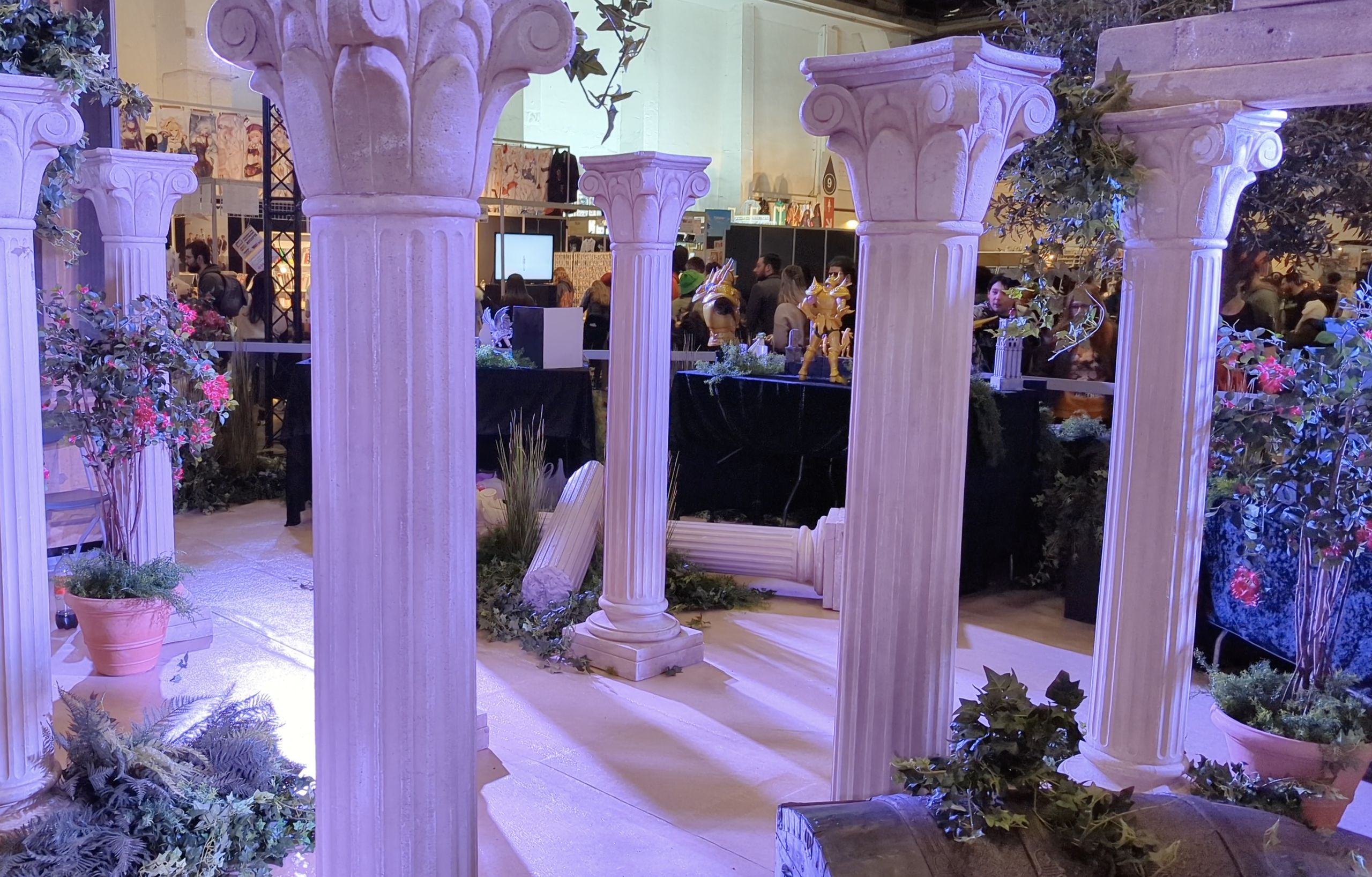 Colonnes grecques et arbustes fleuris du stand, avec des figurines dorées exposées au fond