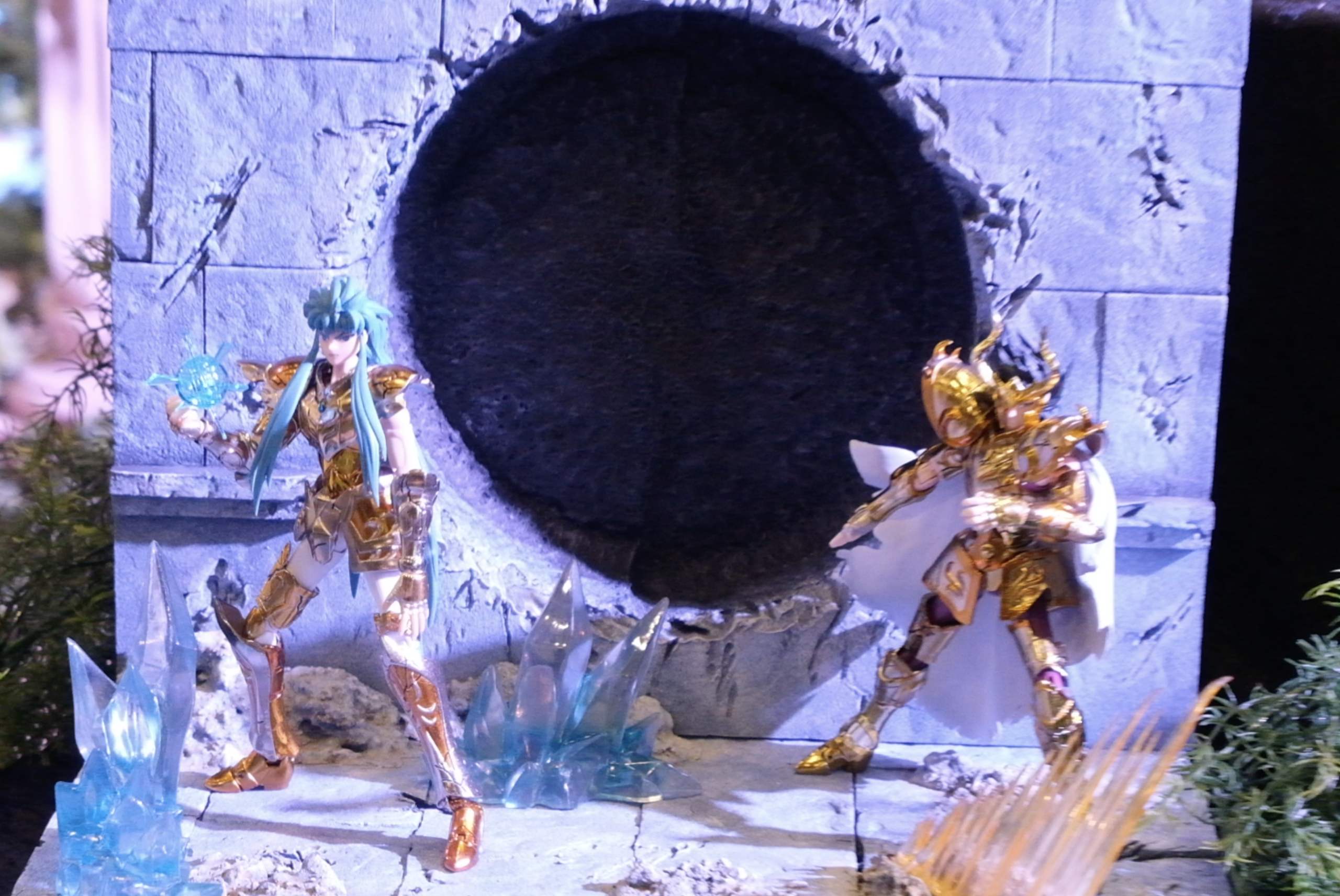 Deux figurines de chevaliers d’or face à face devant un mur percé, entourées de cristaux de glace