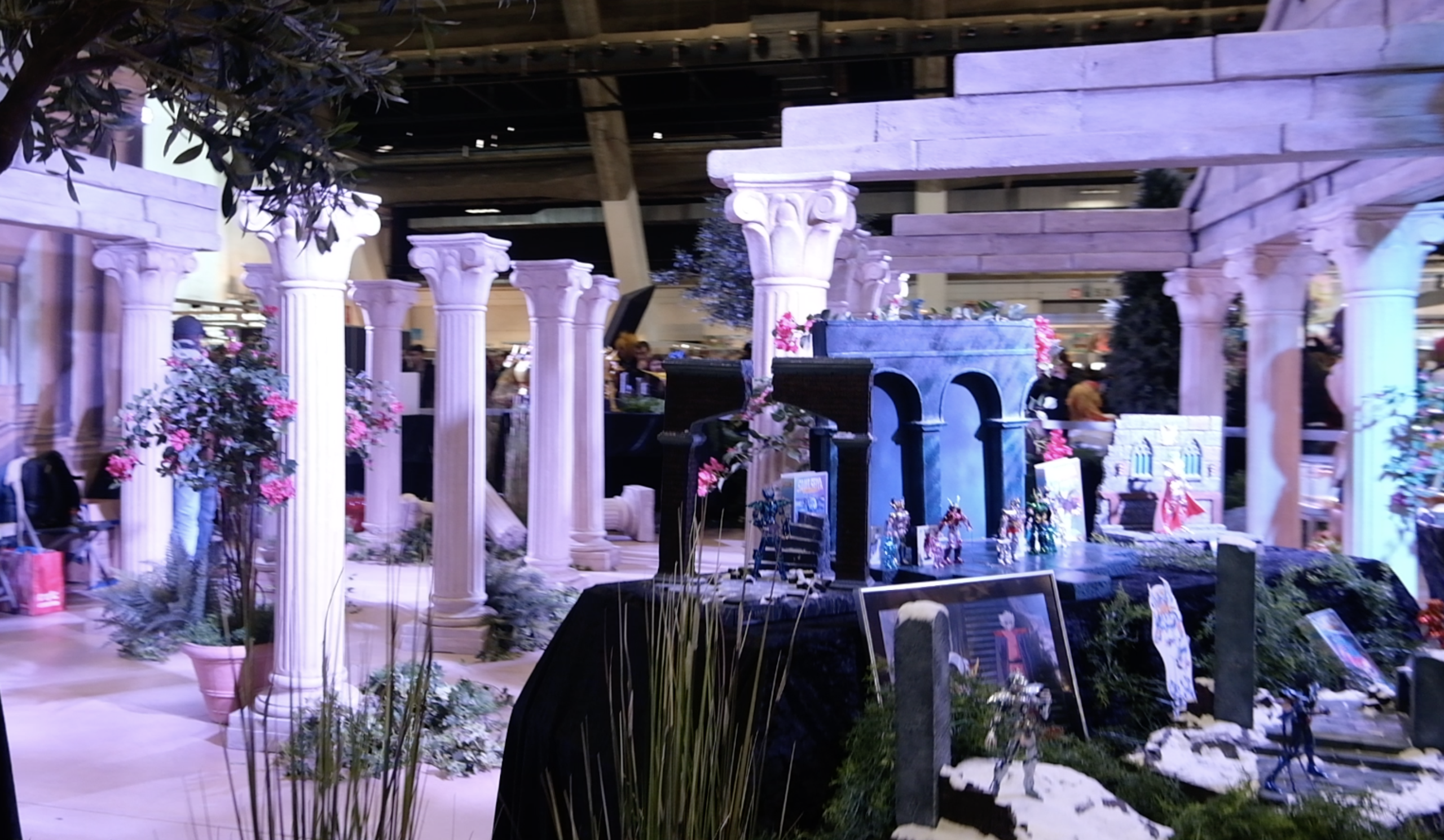 Vue du stand&nbsp;: colonnes grecques, arbustes fleuris et vitrine de figurines Saint Seiya
