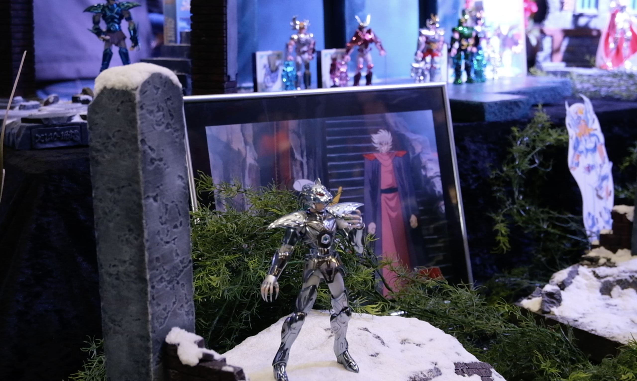 Figurine en armure argentée sur un rocher enneigé, devant un cadre montrant un personnage de l’anime