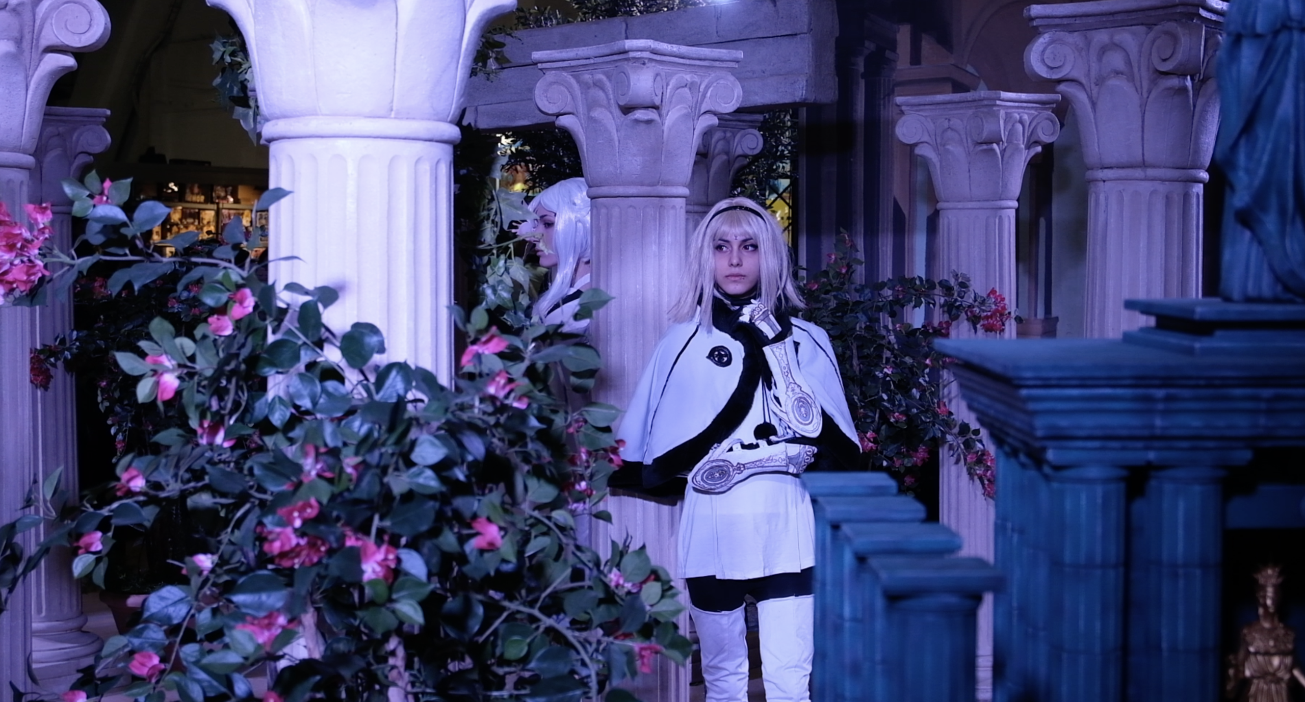 Cosplayeuse en tenue blanche et noire posant entre les colonnes et les fleurs du stand
