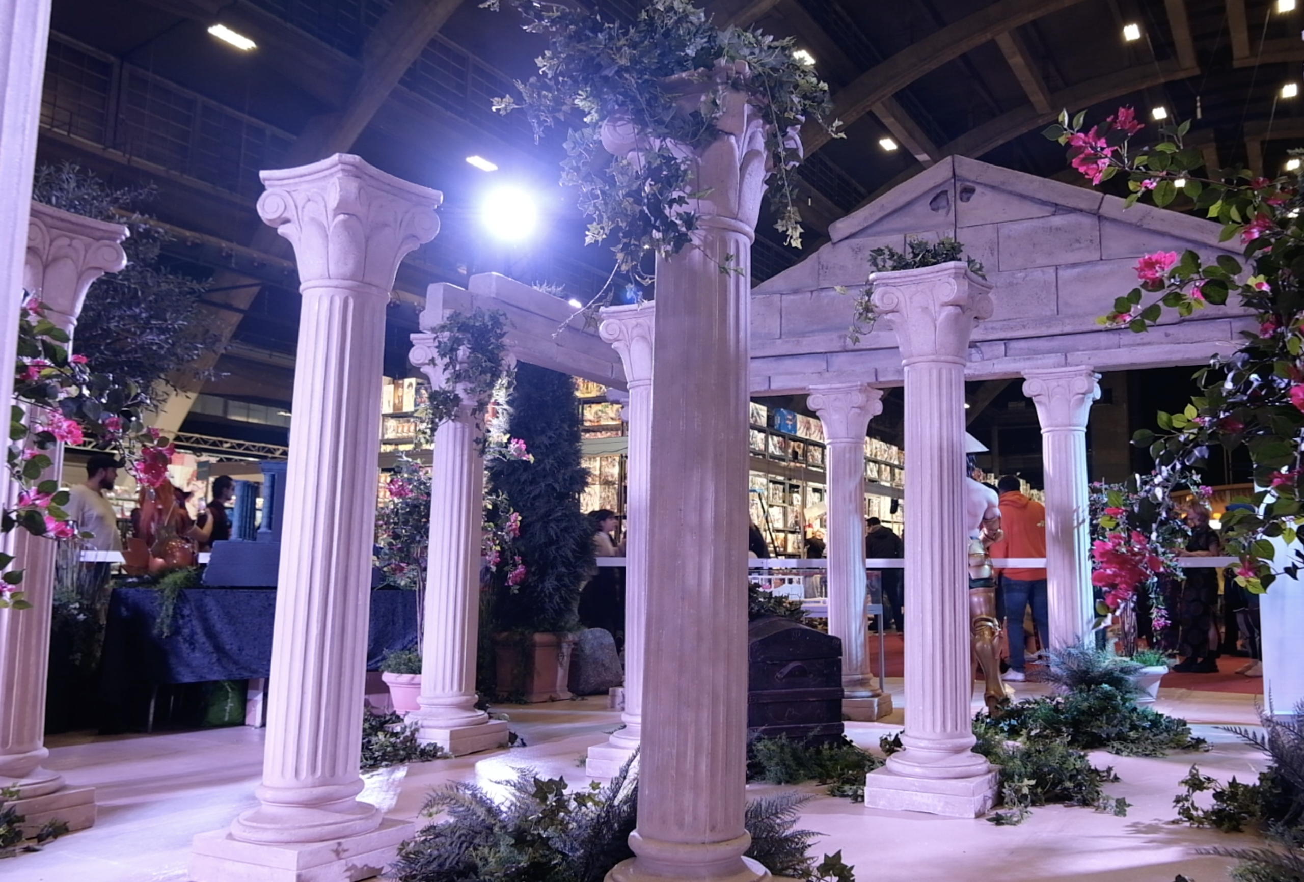 Colonnes grecques couvertes de lierre et malle en bois du stand, sous les projecteurs du salon