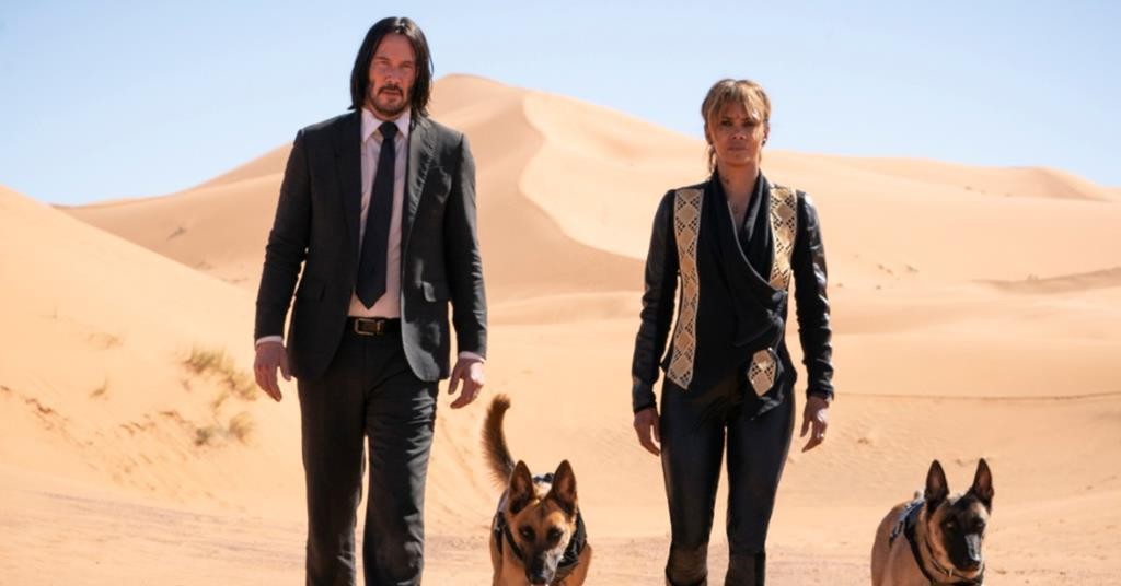John Wick et Halle Berry marchent dans le désert, accompagnés de deux bergers malinois