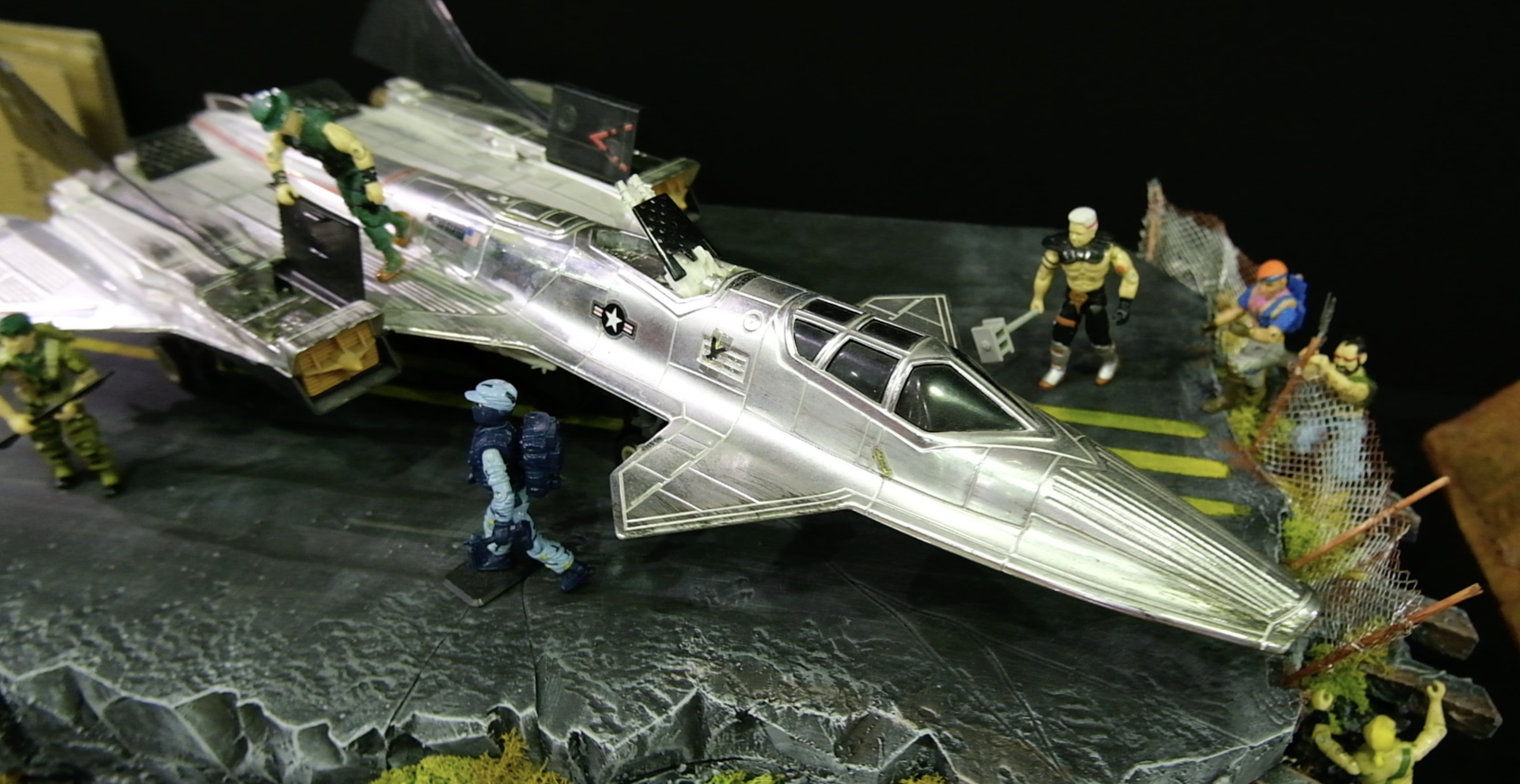 Diorama d’un avion de chasse argenté entouré de figurines militaires sur une piste