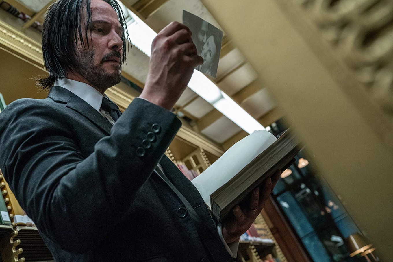 John Wick observe une photo en tenant un vieux livre ouvert dans une bibliothèque