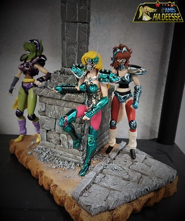 Trois figurines de chevalières masquées de Saint Seiya autour d’une colonne en ruines