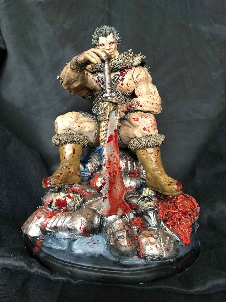 Figurine d’un guerrier assis sur un tas d’armures, une grande épée ensanglantée en main
