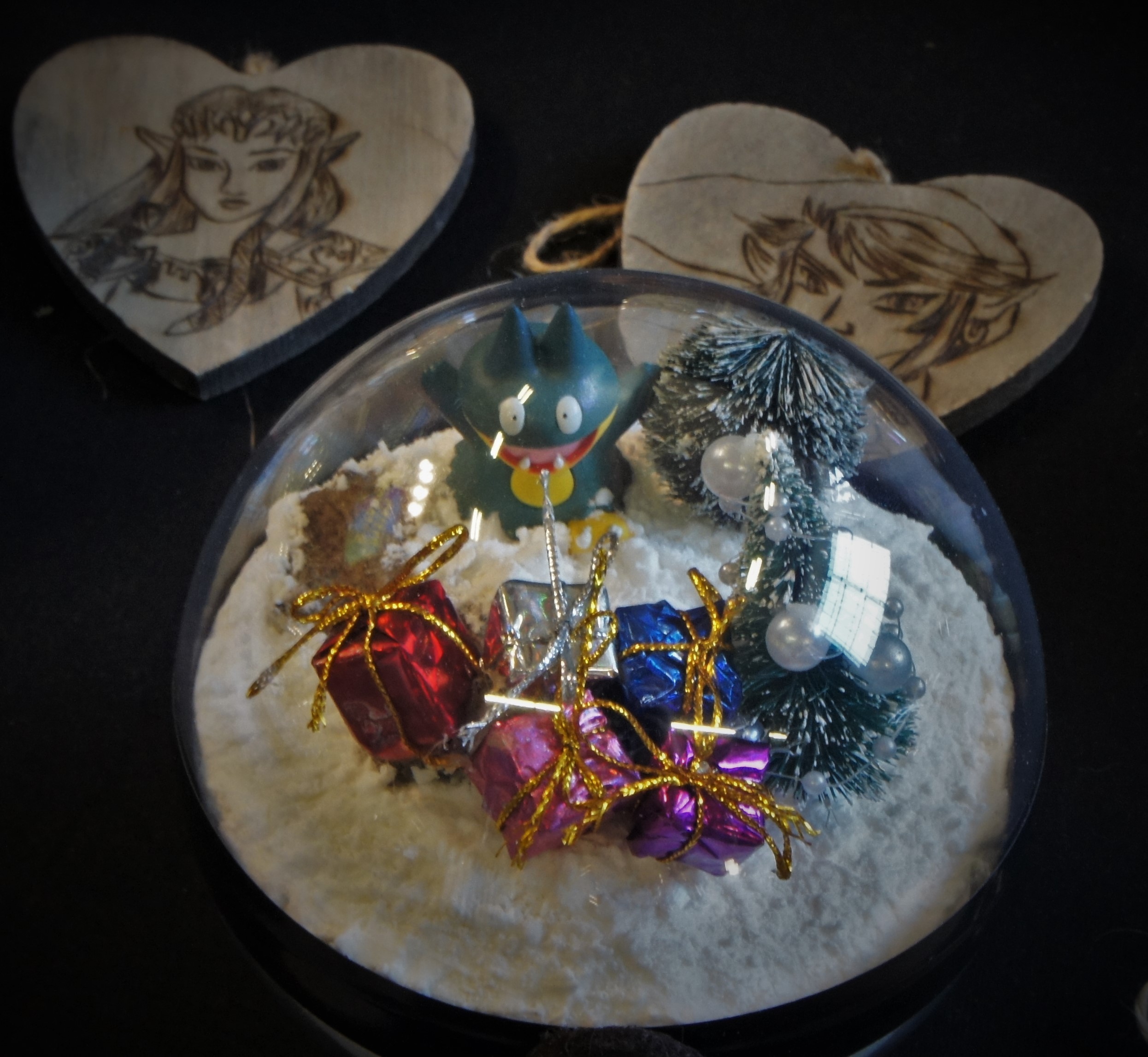 Boule à neige avec un Goinfrex, des cadeaux et un sapin, devant deux cœurs gravés de Zelda et Link