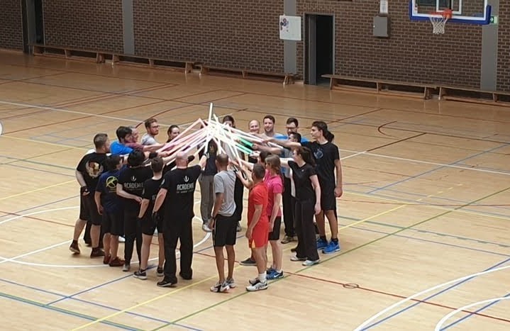 Membres du club réunis en cercle, sabres laser levés au centre d’un gymnase