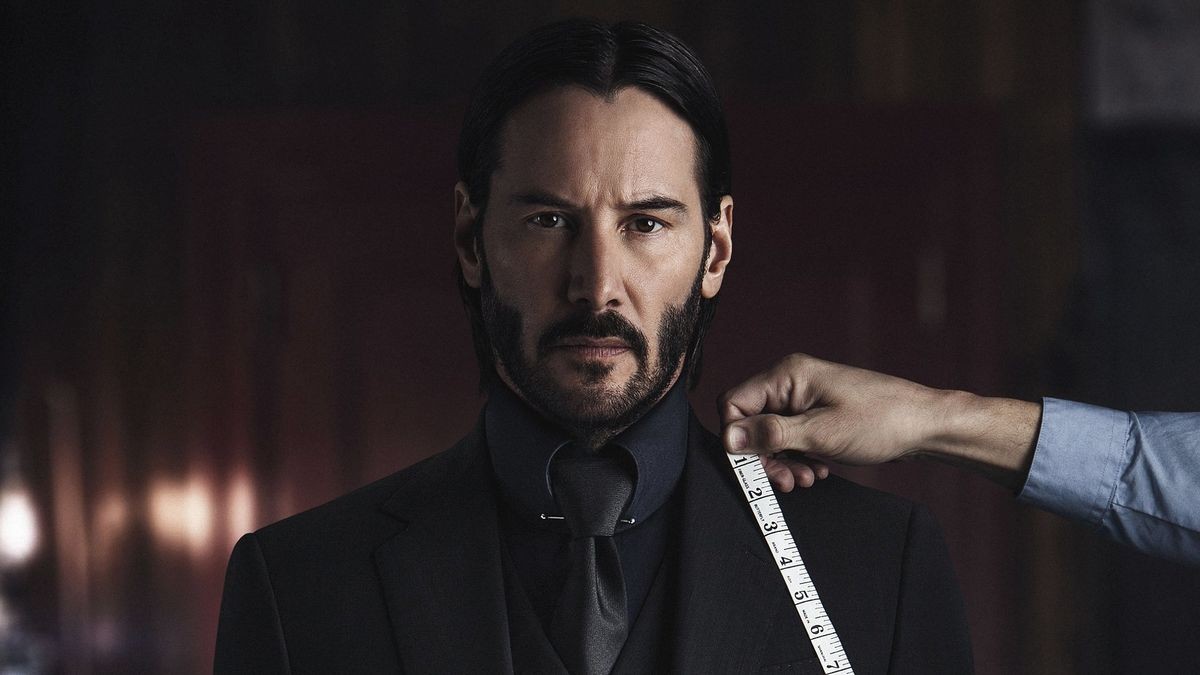 Keanu Reeves en John Wick, regard fixe, pendant qu’un tailleur prend ses mesures
