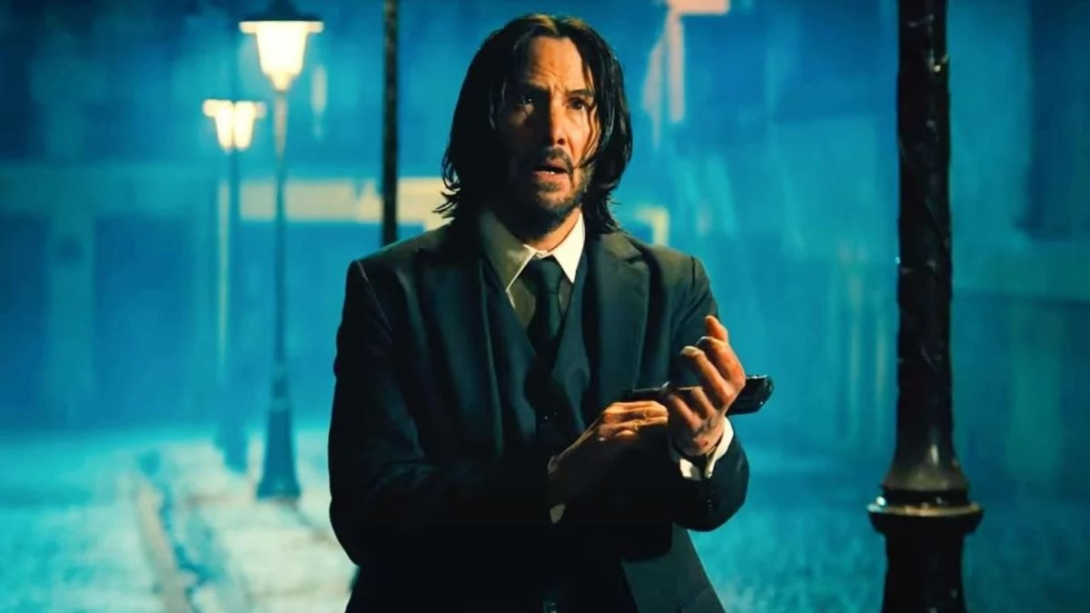 John Wick, inquiet, un téléphone à la main, dans une rue nocturne baignée de lumière bleue