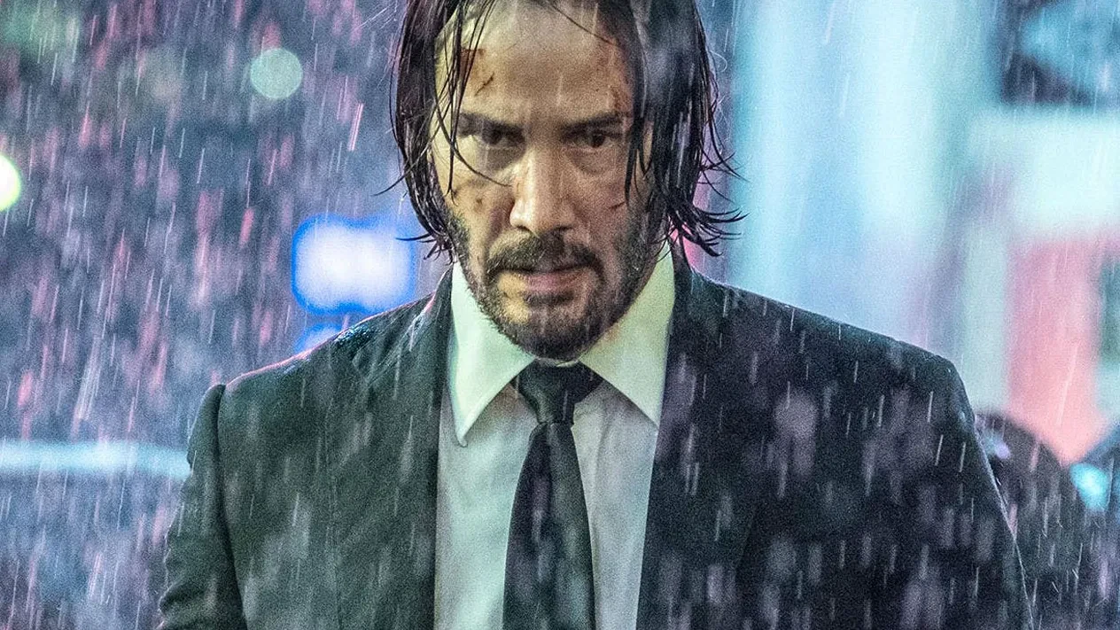 Keanu Reeves en John Wick, trempé et blessé, marchant sous une pluie battante