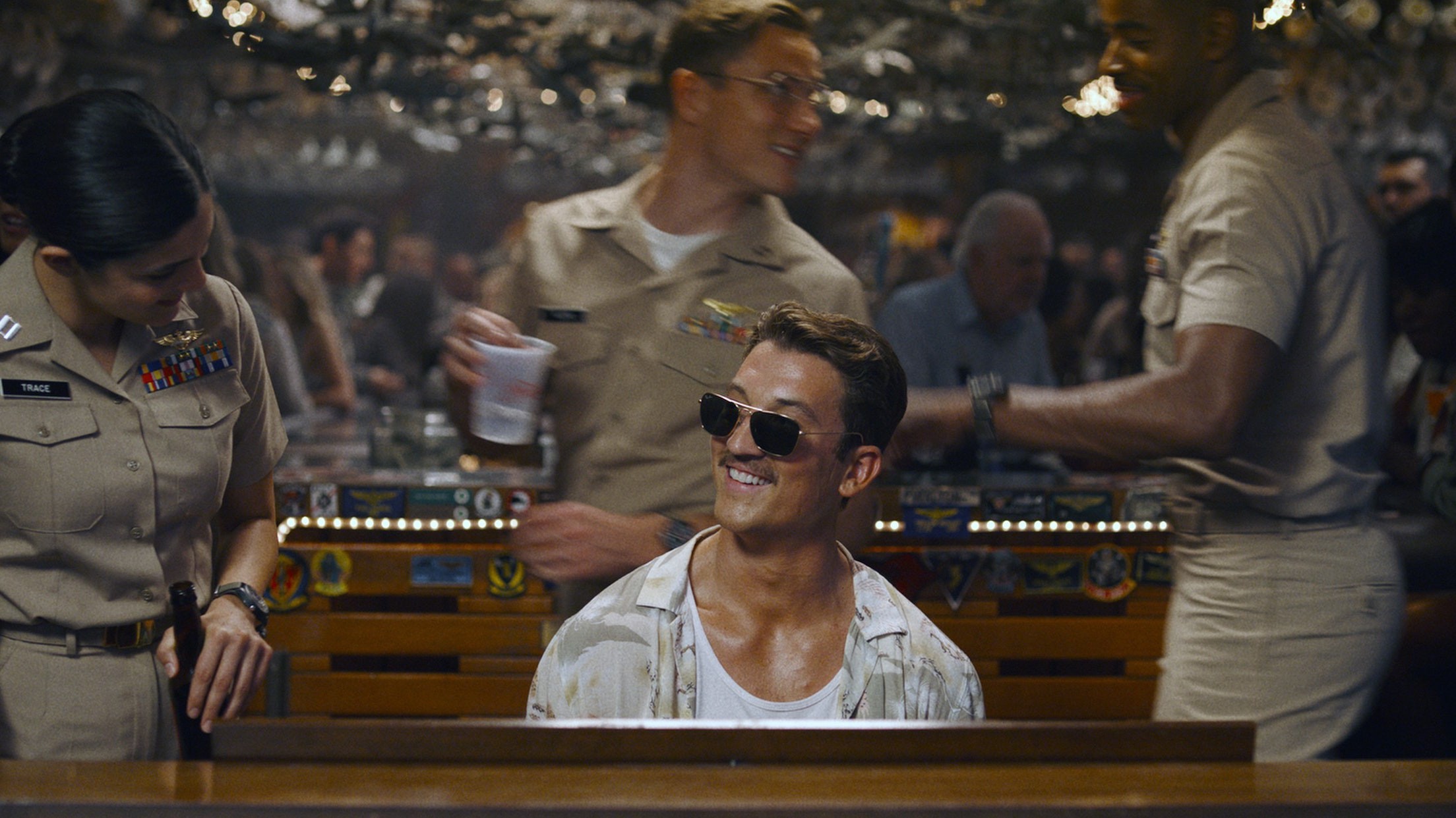 Pilote moustachu en lunettes de soleil, souriant au piano d’un bar plein d’aviateurs