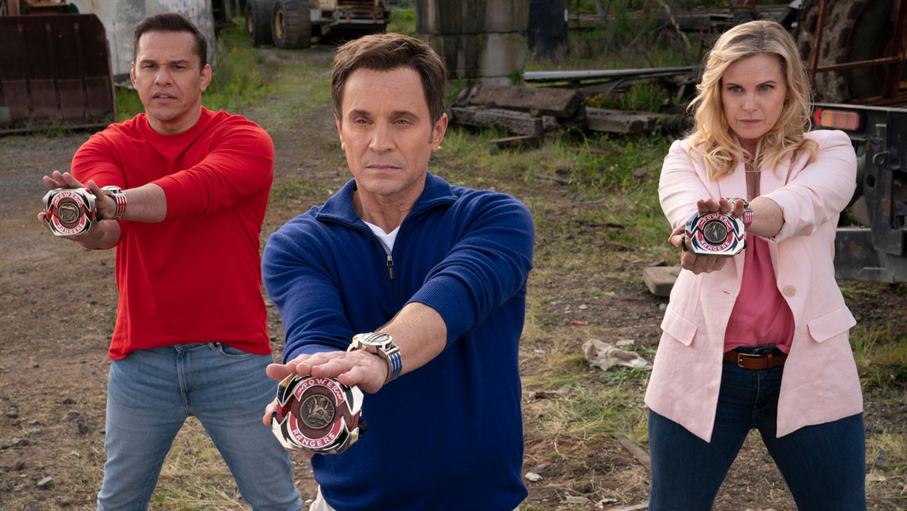 Trois anciens rangers en civil, vêtus de rouge, bleu et rose, tendant leur morpher face caméra