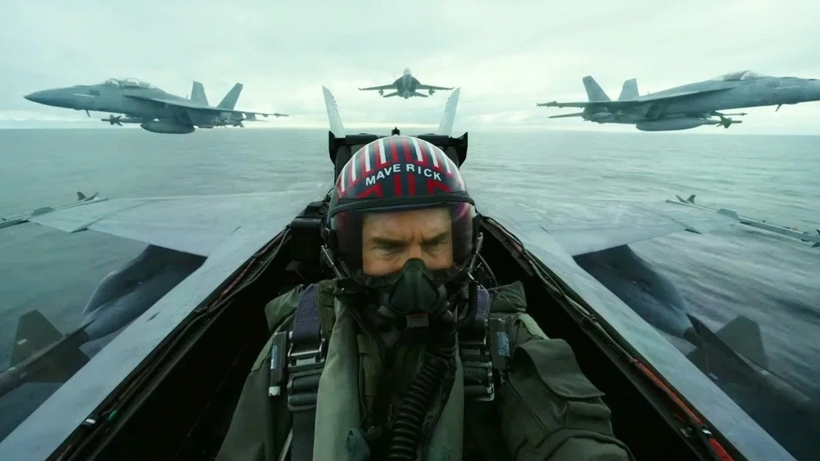 Maverick casqué aux commandes de son avion, escorté par trois chasseurs au-dessus de la mer