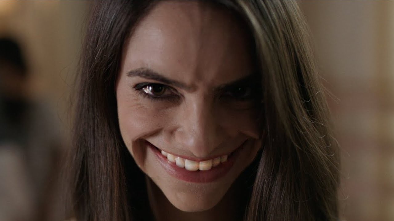 Femme aux cheveux bruns arborant un large sourire menaçant dans Smile