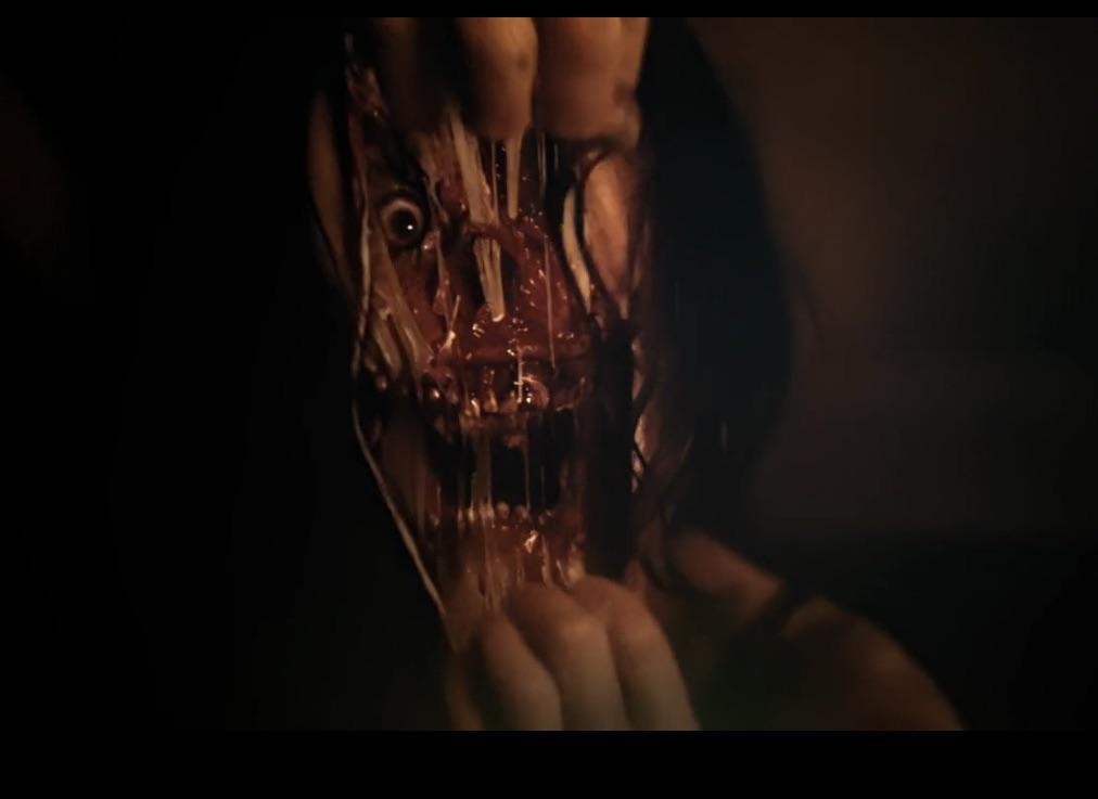 Visage déchiré et sanglant de l’entité de Smile, écarté par deux mains