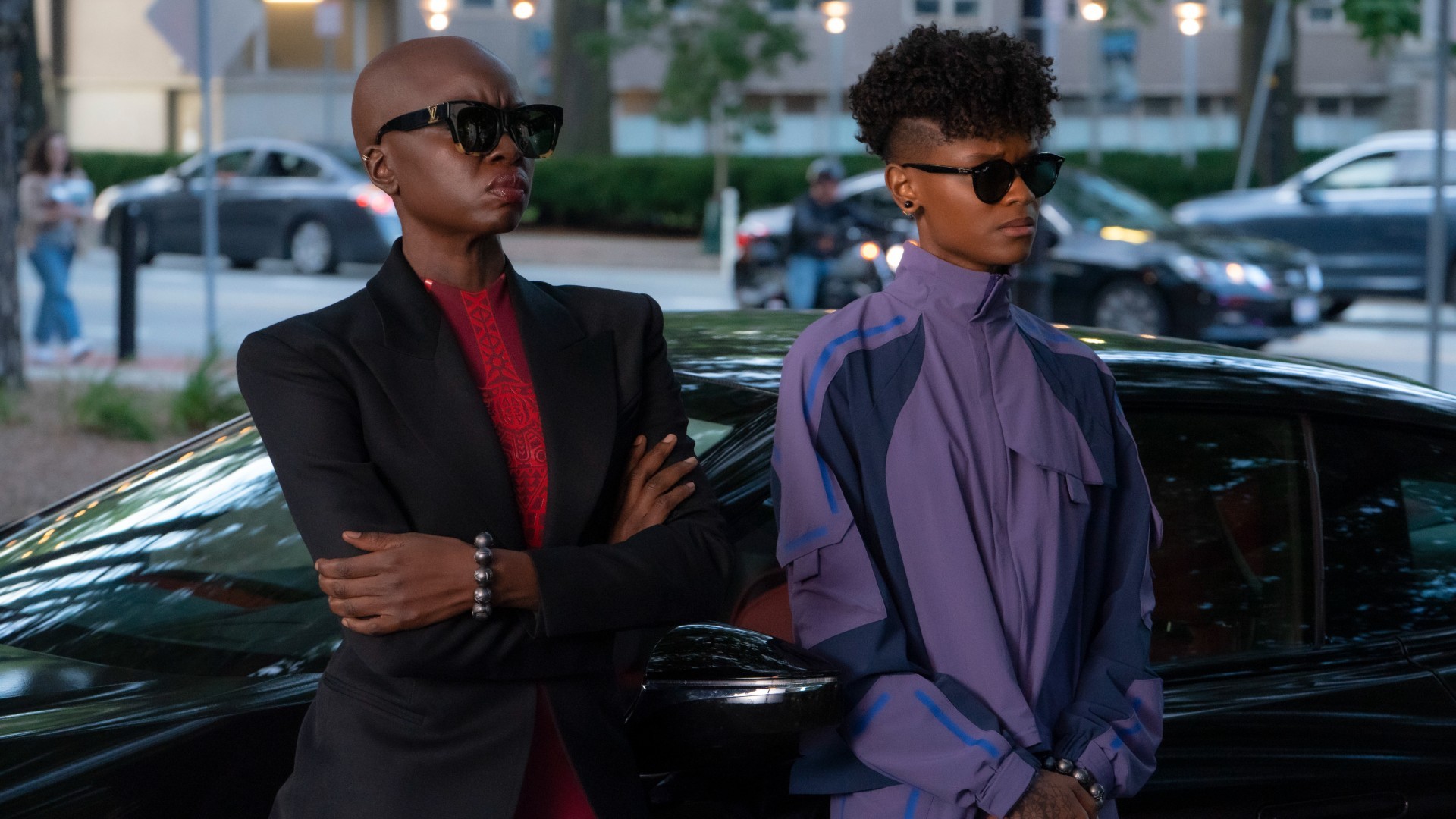 Okoye et Shuri en lunettes de soleil, adossées à une voiture noire