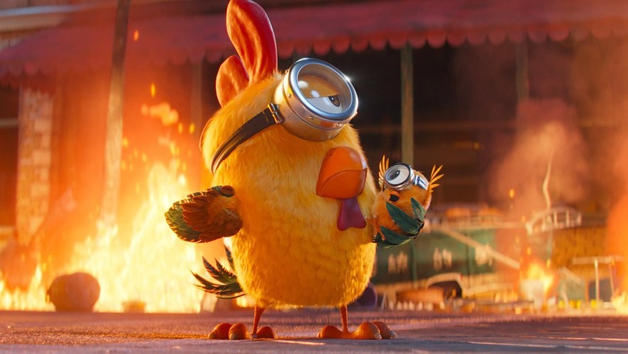 Un Minion déguisé en poussin tient un petit Minion devant un incendie