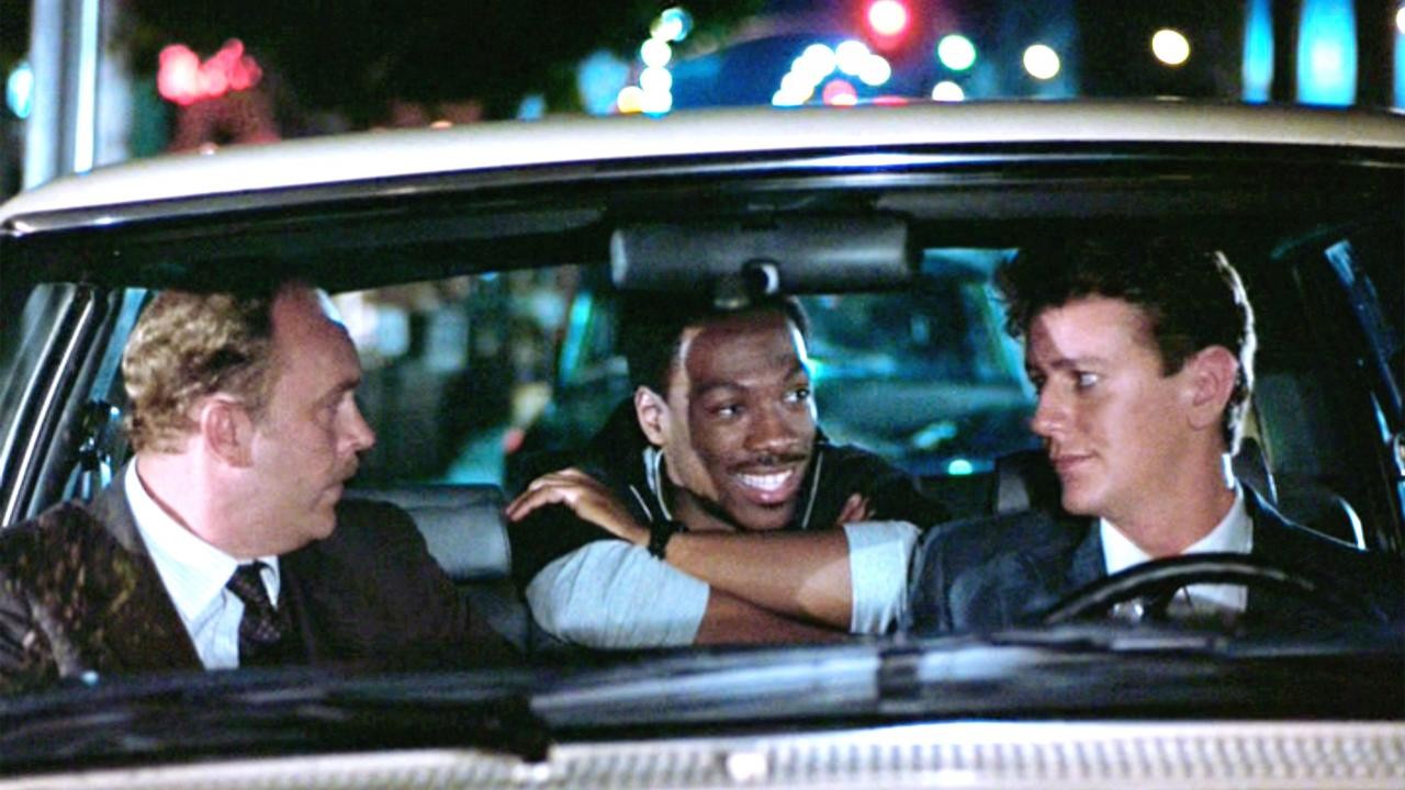 Eddie Murphy souriant entre deux policiers dans une voiture, scène du Flic de Beverly Hills