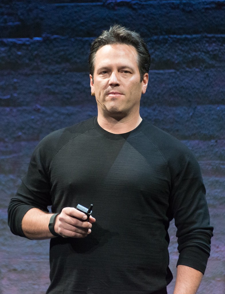 Phil Spencer, patron de Xbox, sur scène en pull noir, une télécommande à la main