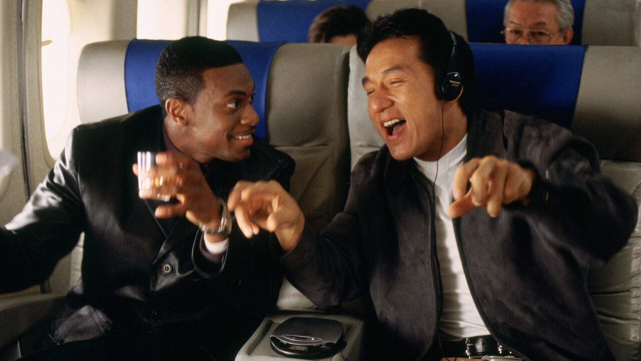 Chris Tucker, un verre à la main, et Jackie Chan, casque sur les oreilles, éclatent de rire dans un avion