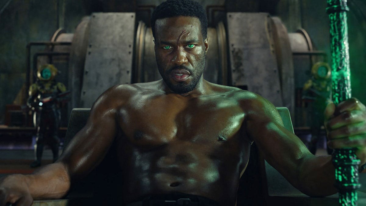 Yahya Abdul-Mateen II en Black Manta, yeux verts luisants, assis la main sur un trident noir