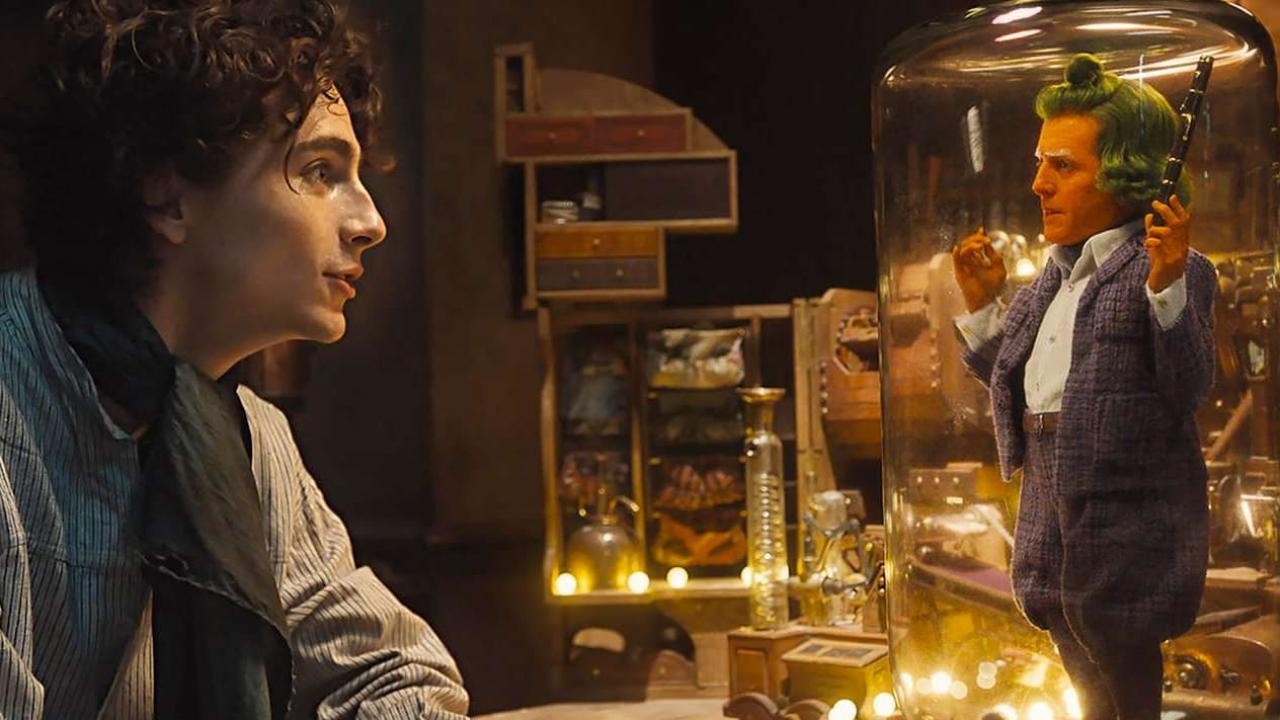 Willy Wonka face à un Oompa-Loompa joué par Hugh Grant, enfermé dans une cloche de verre