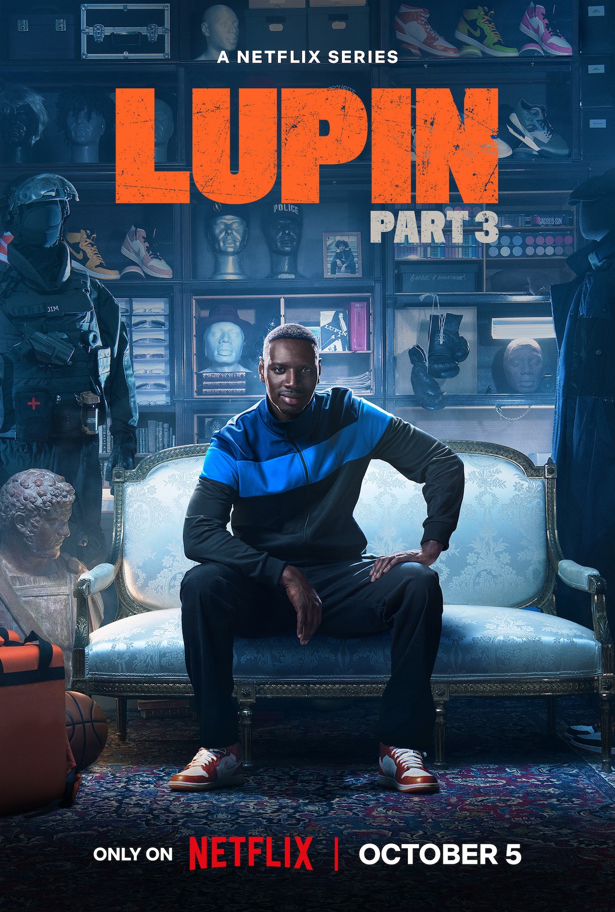 Affiche de Lupin partie 3&nbsp;: Omar Sy assis sur un canapé, en survêtement bleu et noir