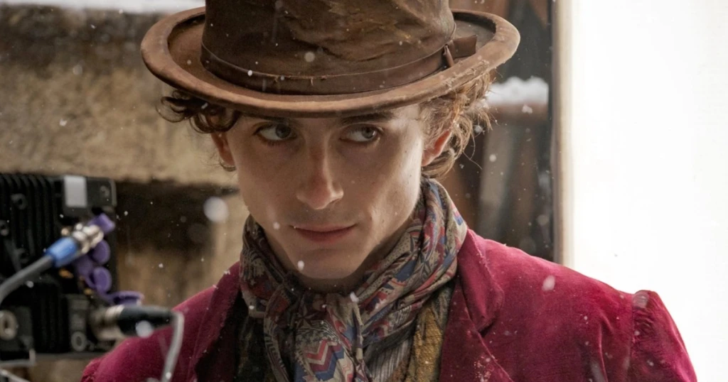 Timothée Chalamet en jeune Willy Wonka, chapeau usé et foulard bariolé, regard en coin