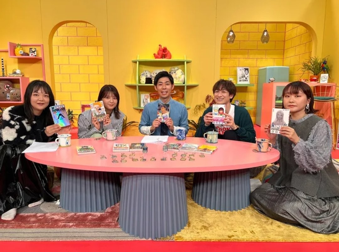 Plateau de l’émission télévisée&nbsp;: cinq présentateurs autour d’une table rose, tenant des tomes de Hunter x Hunter