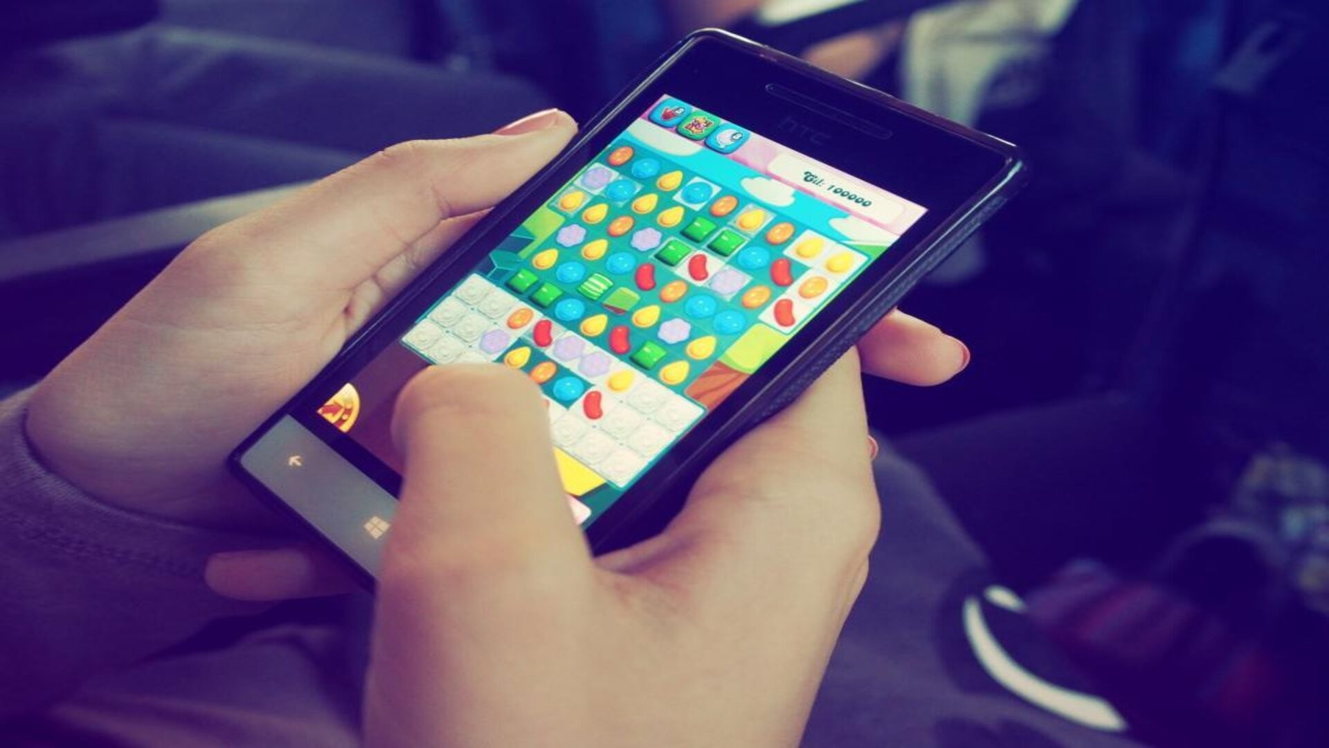Mains tenant un smartphone affichant une partie de Candy Crush Saga