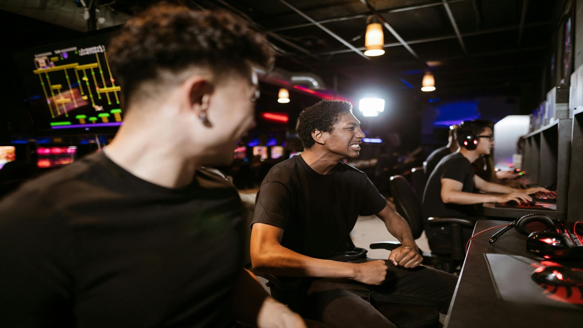 Jeunes joueurs riant ensemble devant des PC dans une salle de jeux en réseau