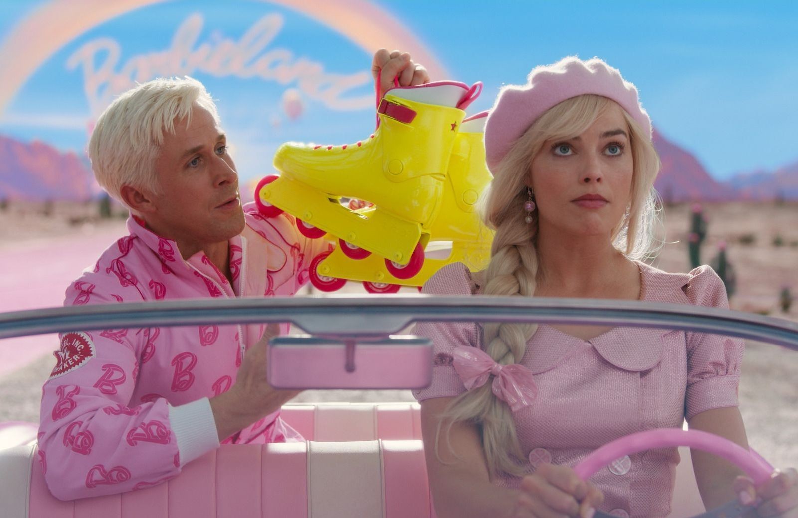 Ken tend des rollers jaunes à Barbie, au volant d’une décapotable rose devant le panneau Barbieland