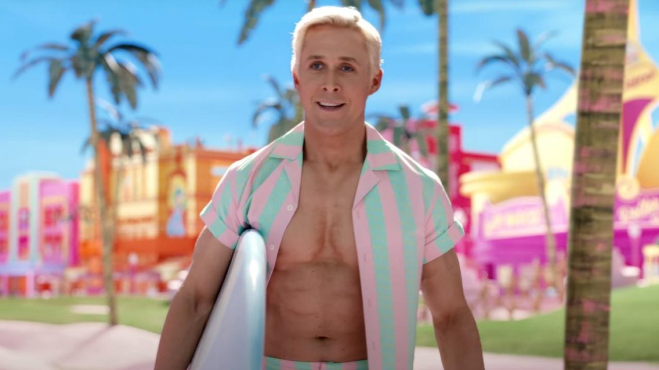 Ryan Gosling en Ken, chemise rayée rose et vert ouverte, planche de surf sous le bras