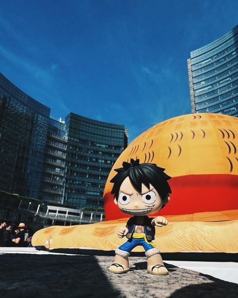 Figurine de Luffy devant un chapeau de paille gonflable géant, au pied de tours vitrées