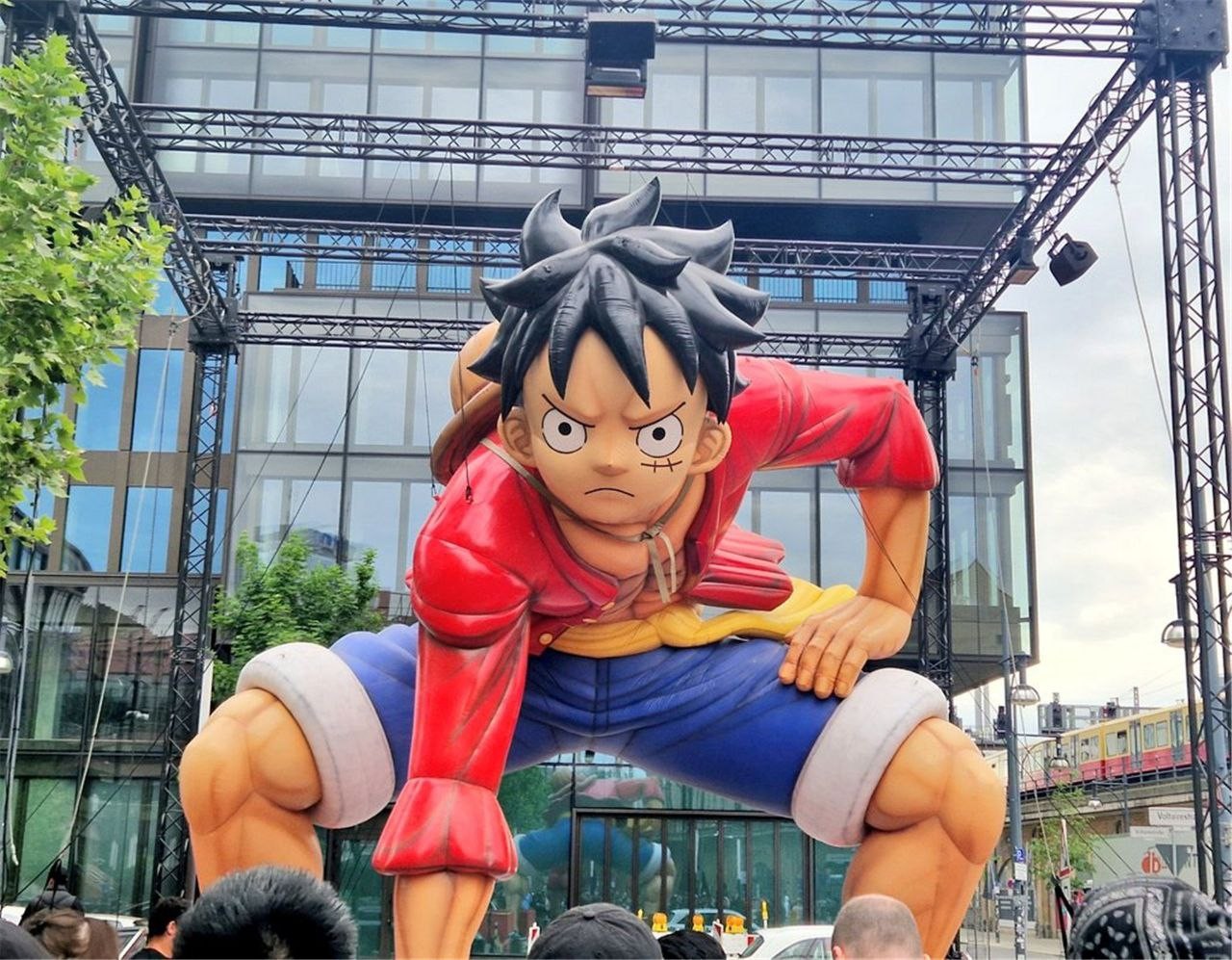 Luffy gonflable géant en position de combat sous un portique, devant un immeuble de verre