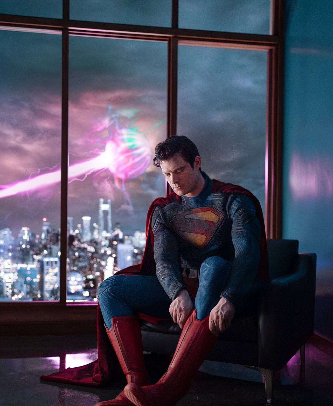 David Corenswet en Superman, assis dans un fauteuil devant une baie vitrée, enfile ses bottes