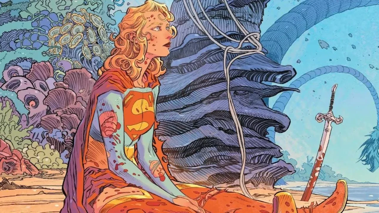 Case de comics&nbsp;: Supergirl blessée, assise sur une plage près d’une épée plantée dans le sable