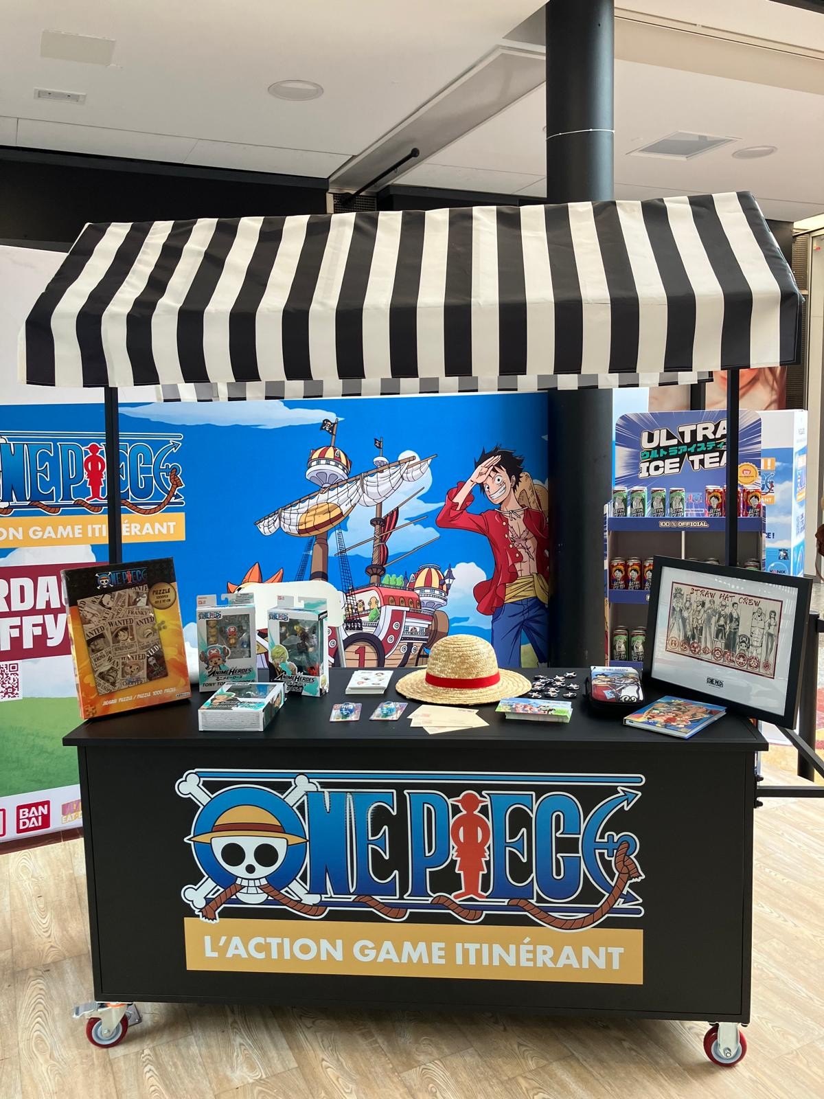Comptoir de produits One Piece sous un auvent rayé, chapeau de paille posé dessus