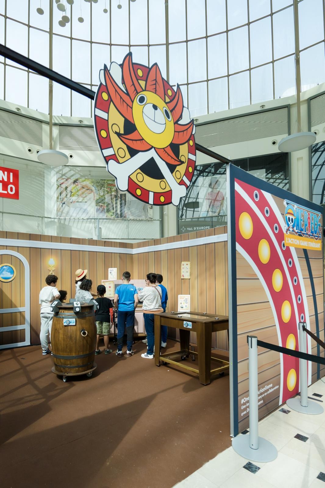 Entrée du One Piece Action Game sous l’emblème du Thousand Sunny, enfants autour d’un tonneau