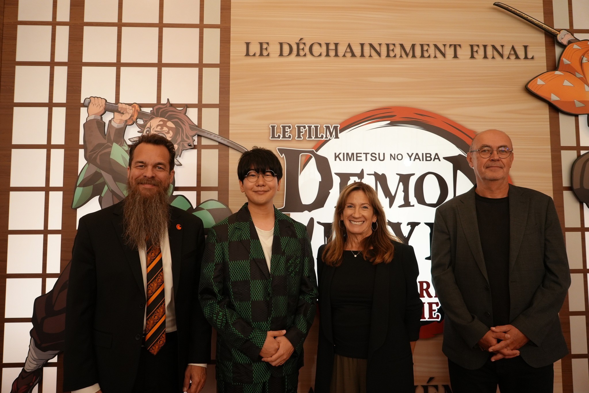 Quatre invités, dont un homme en costume à damier vert façon Tanjiro, devant le décor du film Demon Slayer